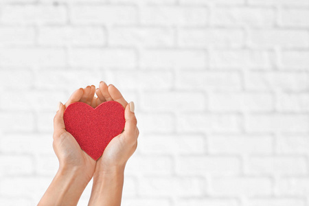 女人抱着红色的心在砖墙的背景上。医疗保健理念