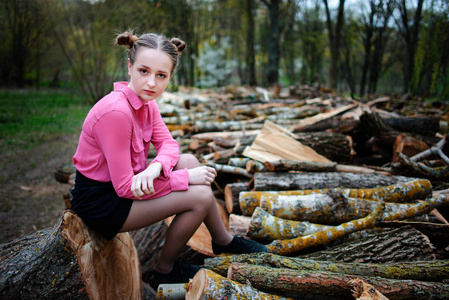 美丽的年轻女子坐在森林里倒下的树干堆栈上