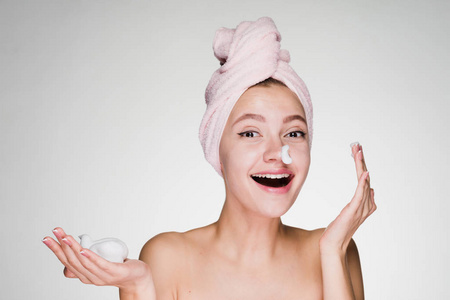 有趣的年轻女孩在她的头上粉红色的毛巾应用洁面泡沫在她的脸上