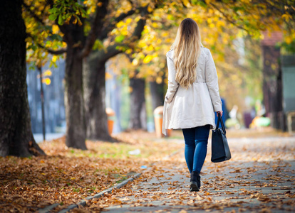 穿着大衣的女人走在美丽的秋城街, 后景色