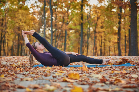 美丽的年轻女子练习瑜伽体式仰卧 Padangushthasana 1 在木甲板上的秋季公园