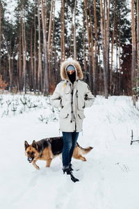 英俊的白种人在冬天夹克在森林里漫步与德国牧羊犬