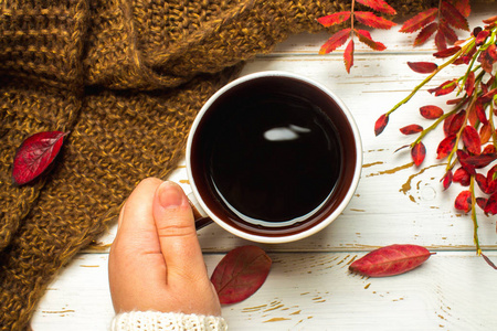 大杯热咖啡在秋天设置与一条围巾，木制的桌子上的一件毛衣在一个女人手里的毛衣。舒适 温馨 舒适