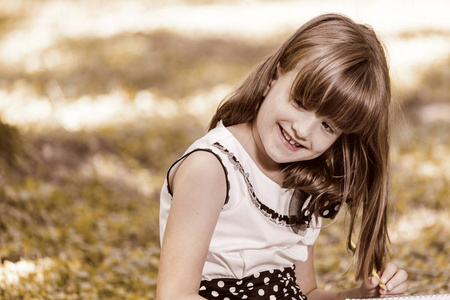 关闭一个甜美的微笑的小女孩的肖像坐在草地上, 户外