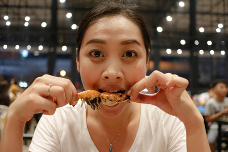 快乐亚洲妇女吃烤虾与美味的咬面