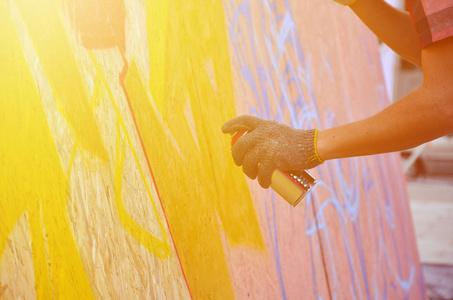 一只手用一种喷雾可以得出新的涂鸦墙上。照片的木墙特写的绘图涂鸦的过程。街头艺术和非法破坏的概念