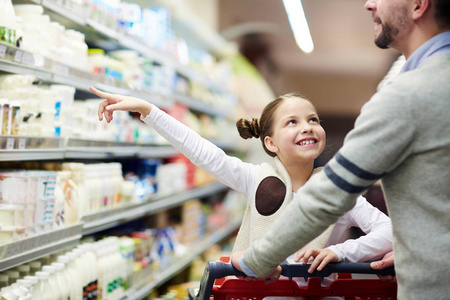 快乐的家庭购买杂货 微笑的小女孩选择乳制品从冰箱在牛奶过道, 而在超市购物