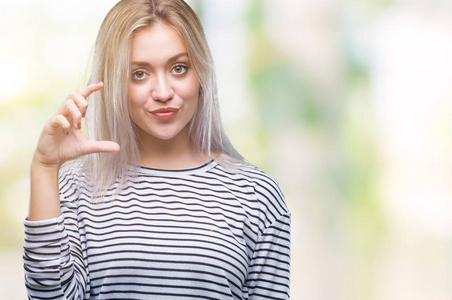 年轻的金发女人在孤立的背景下微笑和自信的手势与手做尺寸符号与手指, 当看和相机。度量概念