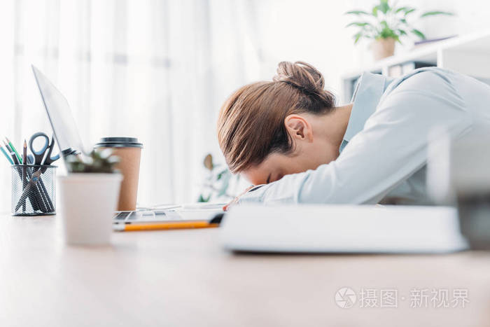 过度劳累的成年女实业家在工作场所睡觉的侧面视图