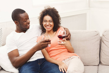 微笑的黑情侣在家里的沙发上喝葡萄酒