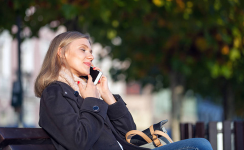 女孩使用手提电话室外坐在长凳上在街道