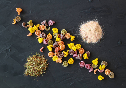 彩色意大利面食的布局与粉红色的喜马拉雅盐和普罗旺斯草药。黑色深色背景和通心粉