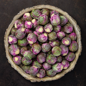 紫色的布鲁塞尔芽在黑暗的背景下的碗里。纯素, 无麸质, 抗过敏, 清洁饮食或生食。旧的深色背景和顶部视图