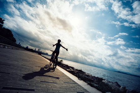 手自由骑自行车的妇女骑山地自行车在日出海滨