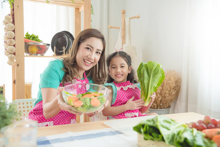 美丽的亚洲母亲和女儿穿着粉红色的围裙烹饪早餐在厨房