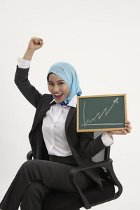 马来商业妇女坐在办公室的椅子上, 拿着图表举着黑板