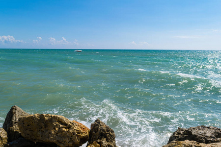 背景蓝绿色海浪海浪在一个明亮的黄色石头。蓝色的大海和喷雾在阳光明媚的一天在岸上, 和游艇离开, 放松