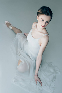 迷人的芭蕾舞演员坐在白色的礼服和芭蕾舞鞋