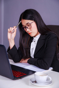 商务妇女坐在办公桌上与笔记本电脑和思考