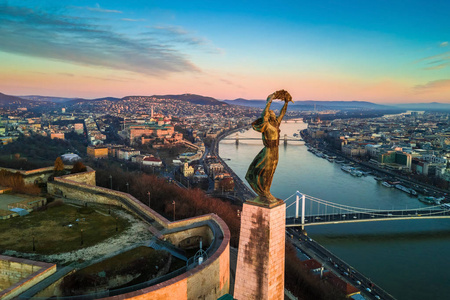 布达佩斯, 匈牙利自由女神像与布达城堡皇宫和链桥背景的空中地平线观。清晨的日出与蓝天白云