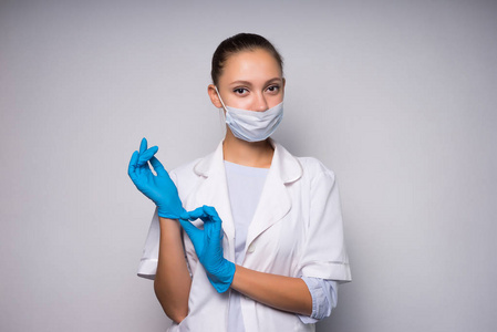 可爱的年轻女医生在保护性医疗面罩戴上手套