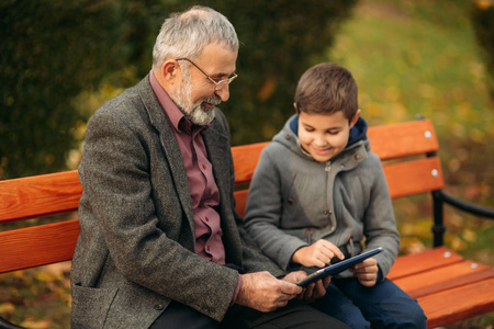 爷爷和他的孙子在公园里一起度过时光。他们坐在长凳上。漫步在公园, 欢庆