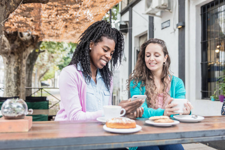两个漂亮的年轻女人看手机, 喝咖啡和吃蛋糕