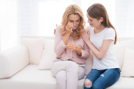 这个女孩安慰一个哭闹的成年妇女。他们坐在家里的沙发上。青少年拥抱她的母亲