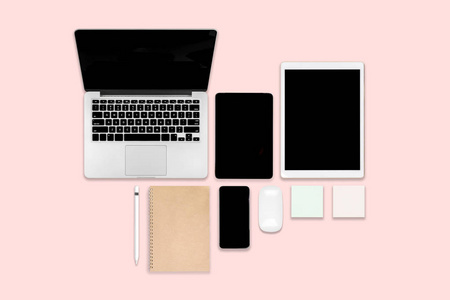 平躺照片的办公桌上有笔记本电脑, 数码片, 手机和配件。在现代粉红色色调的背景。台式机办公室样机概念