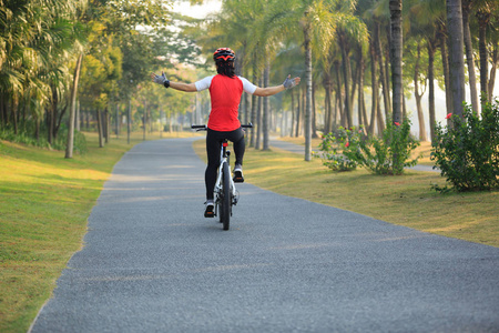 骑自行车的女骑单车在热带公园伸展双臂