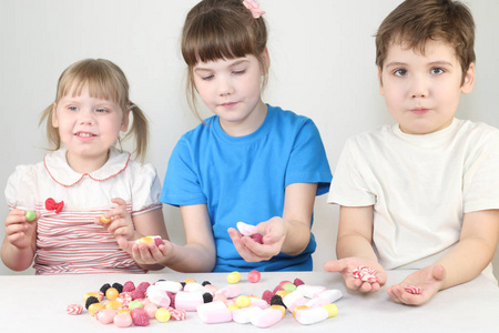 三快乐的孩子坐在餐桌上的糖果和棉花糖
