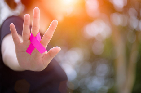 妇女手持有粉红色丝带在绿色背景下支持乳腺癌意识月活动