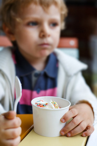 可爱小男孩吃冷冻的酸奶冰激淋在咖啡馆