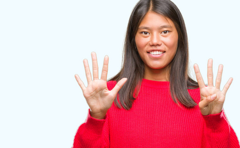 年轻的亚洲妇女穿着冬季毛衣在孤立的背景显示和指向手指九, 而微笑着自信和快乐