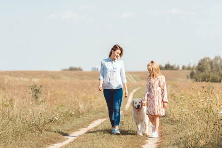 快乐的母亲和女儿走在田野上的金色猎犬