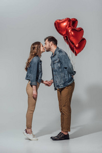 年轻夫妇接吻的侧面看, 而男子抱着红色的心形气球孤立在灰色
