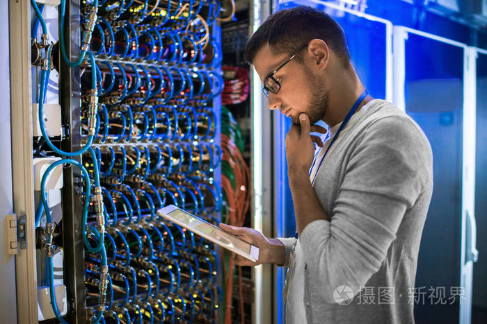 年轻网络工程师的侧面图在数据中心与服务器一起工作时, 若有所思地