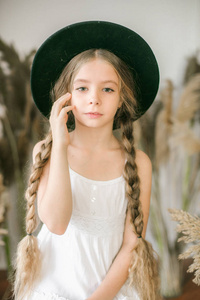 一个可爱的小女孩, 长着金色的头发, 在白色的 sarafan 和一顶草帽在藤椅和芦苇装饰