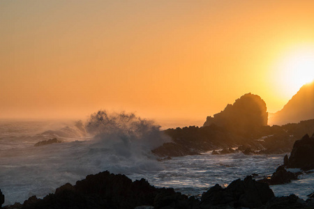 海洋日落与波浪打破到剪影岩石