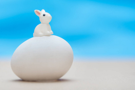 小白玩具兔子坐在一个蓝色背景上的大白鸡蛋上