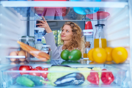 从冰箱里拿食物的女人。从冰箱内部拍摄的照片