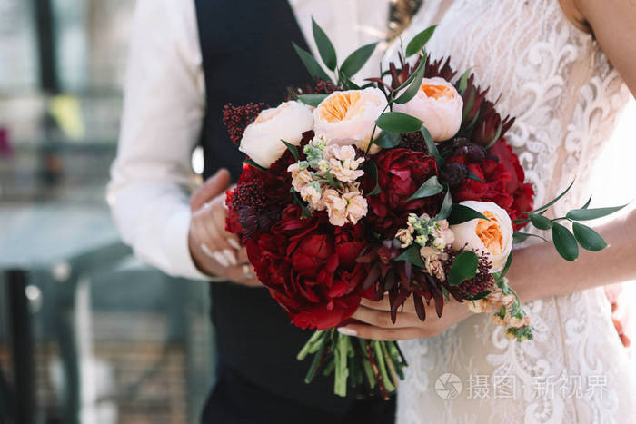 新婚夫妇在她手里捧着牡丹,玫瑰,红花和绿叶的结婚花束.