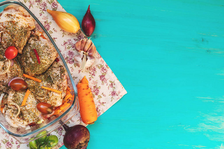 生鲜鸡腿, 配香料和蔬菜在一个玻璃碗里。许多食物成分在浅蓝色木背景。顶部视图, 景深, 色调和处理照片