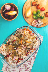 生鲜鸡腿, 配香料和蔬菜在一个玻璃碗里。许多食物成分在浅蓝色木背景。顶部视图, 景深, 色调和处理照片