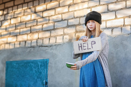 无家可归的贫穷少女拿着空碗和一块纸板与 word 帮助户外