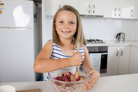 年轻美丽和可爱的女孩6或7岁烹饪和烘烤在家里厨房准备草莓蛋糕与碗微笑愉快和自信