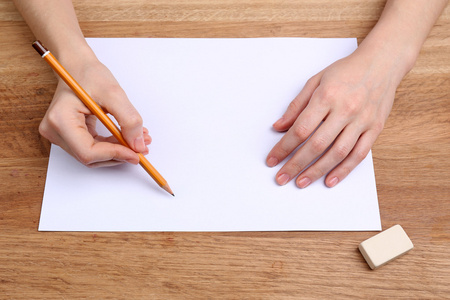 人类的手，用铅笔写在纸张和擦除橡胶木桌背景