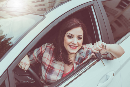 微笑的妇女坐在新车和显示汽车钥匙