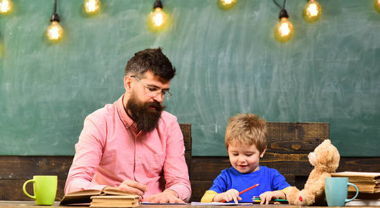 老师和小孩子写信在抄写本。可爱的男孩画一幅五颜六色的铅笔画。幼儿园美术课