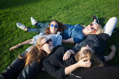一群快乐的微笑无忧无虑的年轻时尚女孩躺在草地上的公园, 千禧年概念, 青年和学生, 旅游和节假日